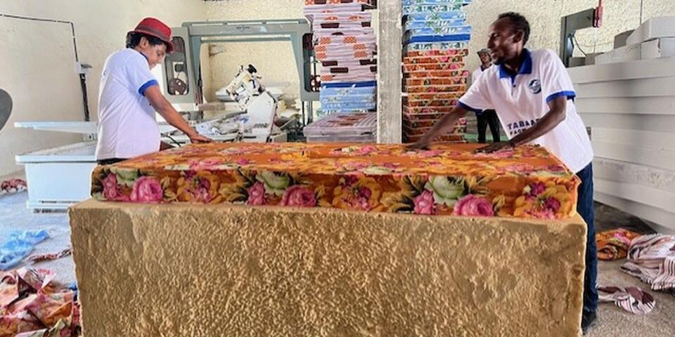2 men manufacturing a mattress standing opposite one another inside a foam factory